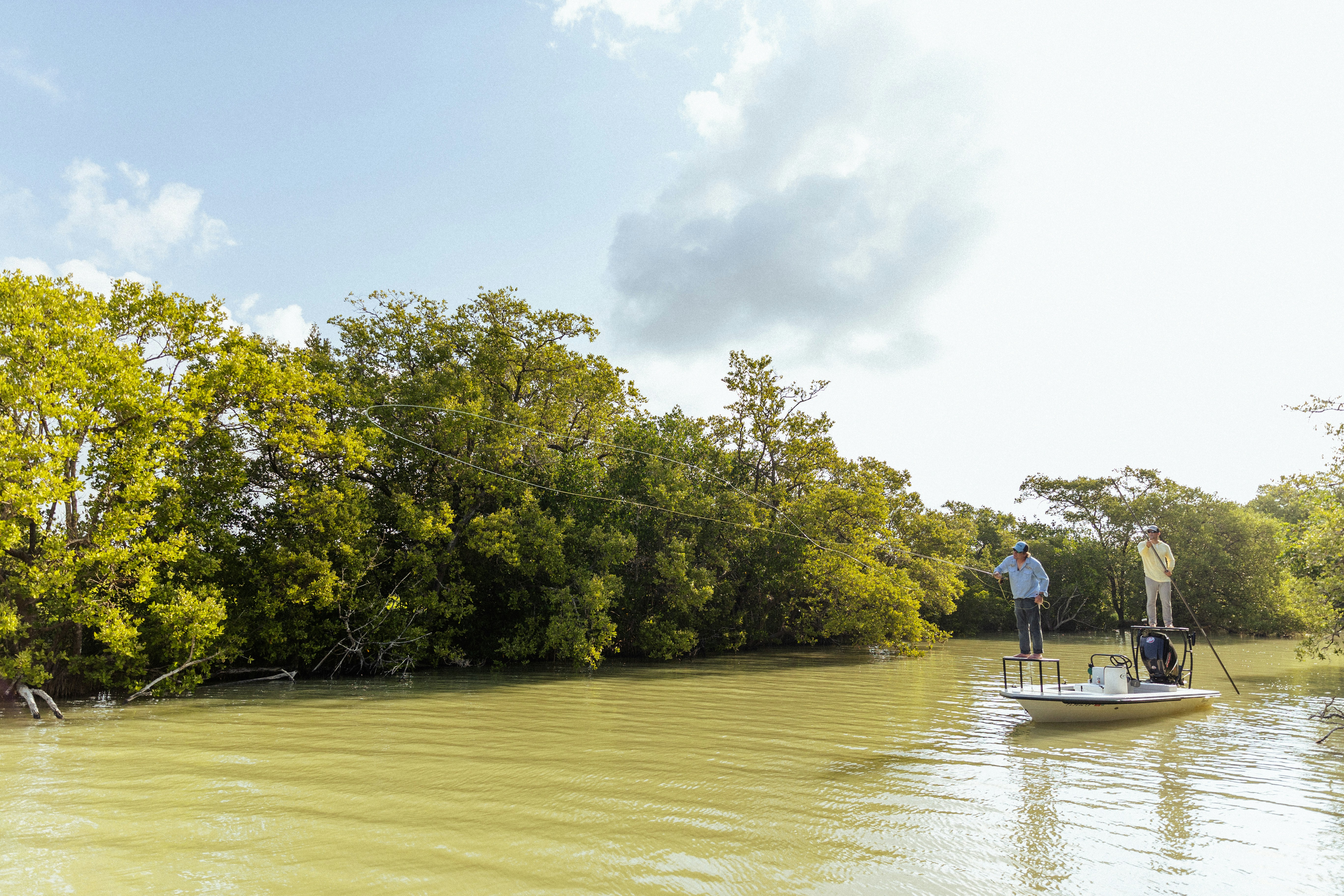 Group of anglers on boat in tropical river, fishing together, green jungle banks